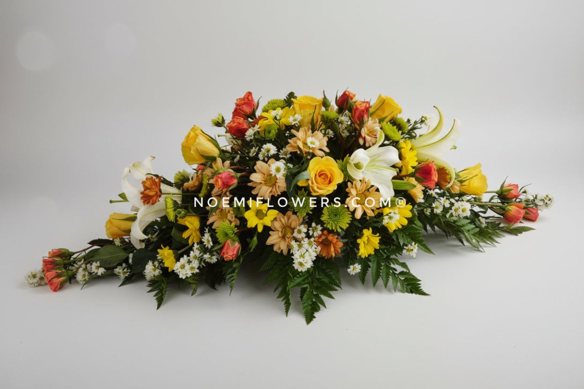 Centro de mesa mediano que combina rosas, lirios y flores variadas con follaje seleccionado, presentado en base plana - Floristería Noemi Flowers