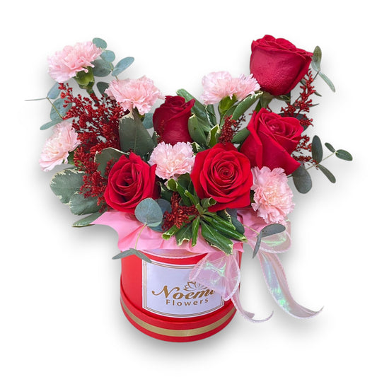 Caja de rosas y claveles con follaje y lazo - Floristería Noemi Flowers.