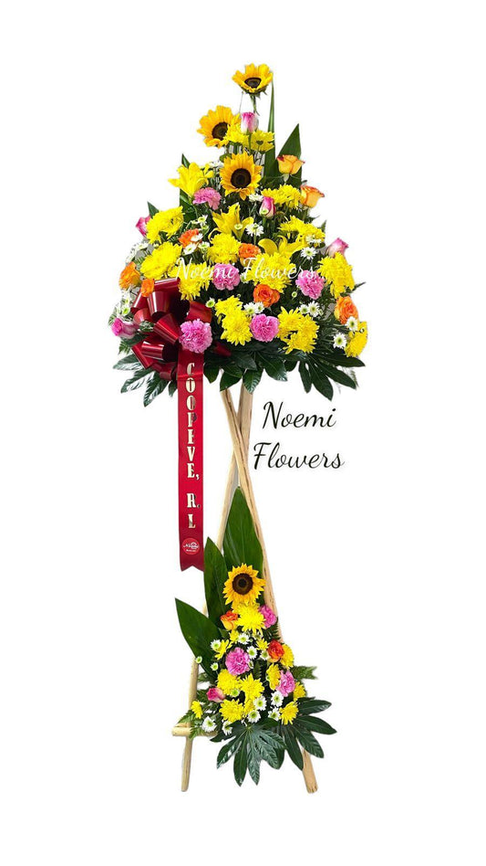 Pedestal en hermosa combinación primaveral con girasoles, rosas, claveles, margaritas, lirios y follaje variado, con lazo.- Floristería Noemi Flowers
